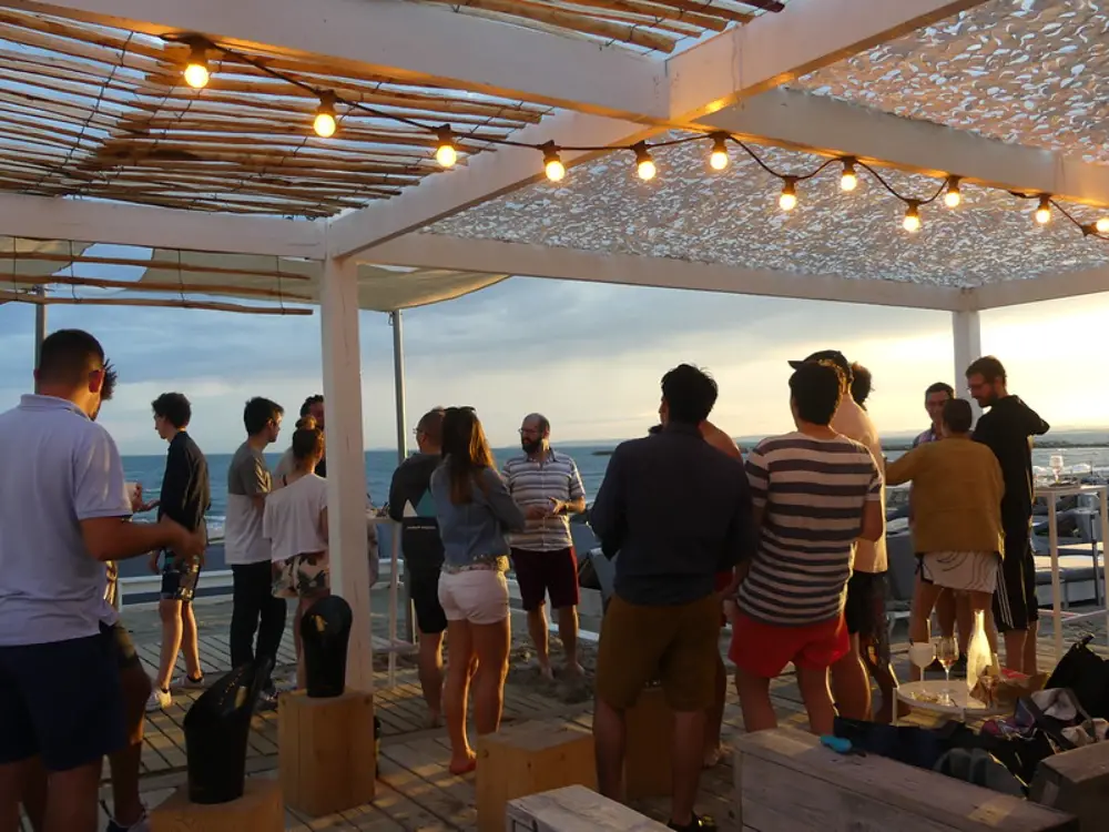 Groupe de collègues en afterwork sur une terrasse en bois face à la mer au coucher du soleil