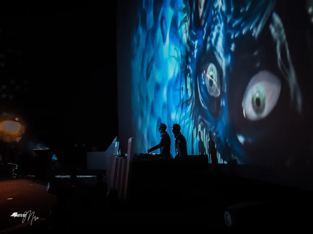 Deux DJ jouent en live devant une projection géante d'animation visuelle aux tons bleus et mystérieux.