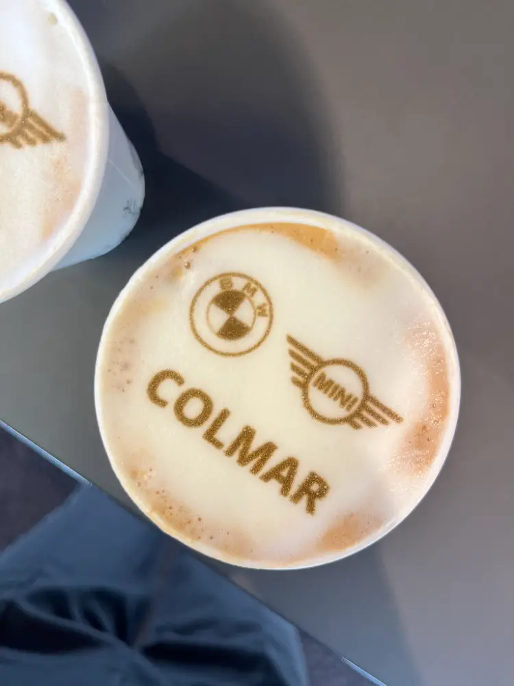 Latte art personnalisé avec les logos BMW et MINI Colmar imprimés à la surface d’un cappuccino, pour un accueil client ultra soigné