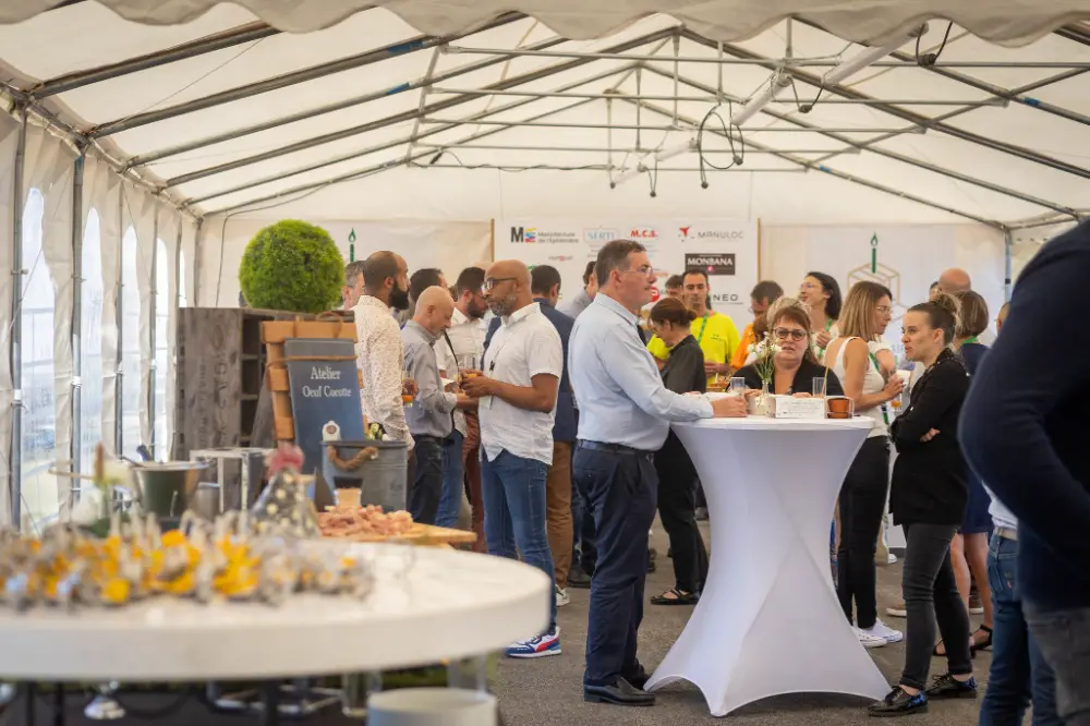 Participants échangeant autour de tables hautes lors d’un cocktail professionnel sous un chapiteau, ambiance détendue et networking actif.
