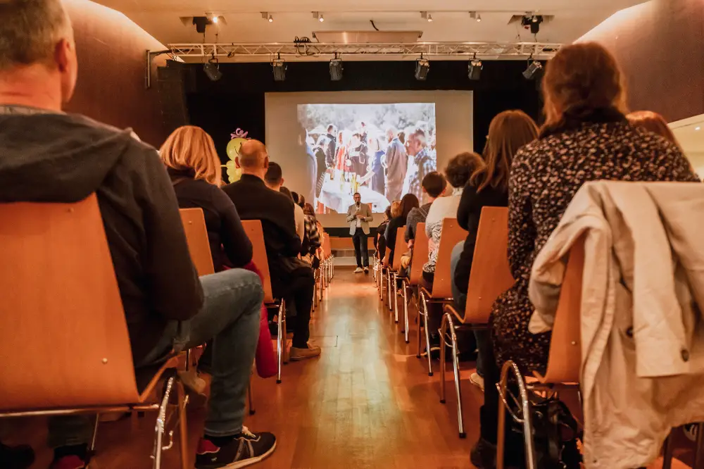 Un intervenant s'adresse à un public assis dans une salle de conférence avec une grande projection en fond.