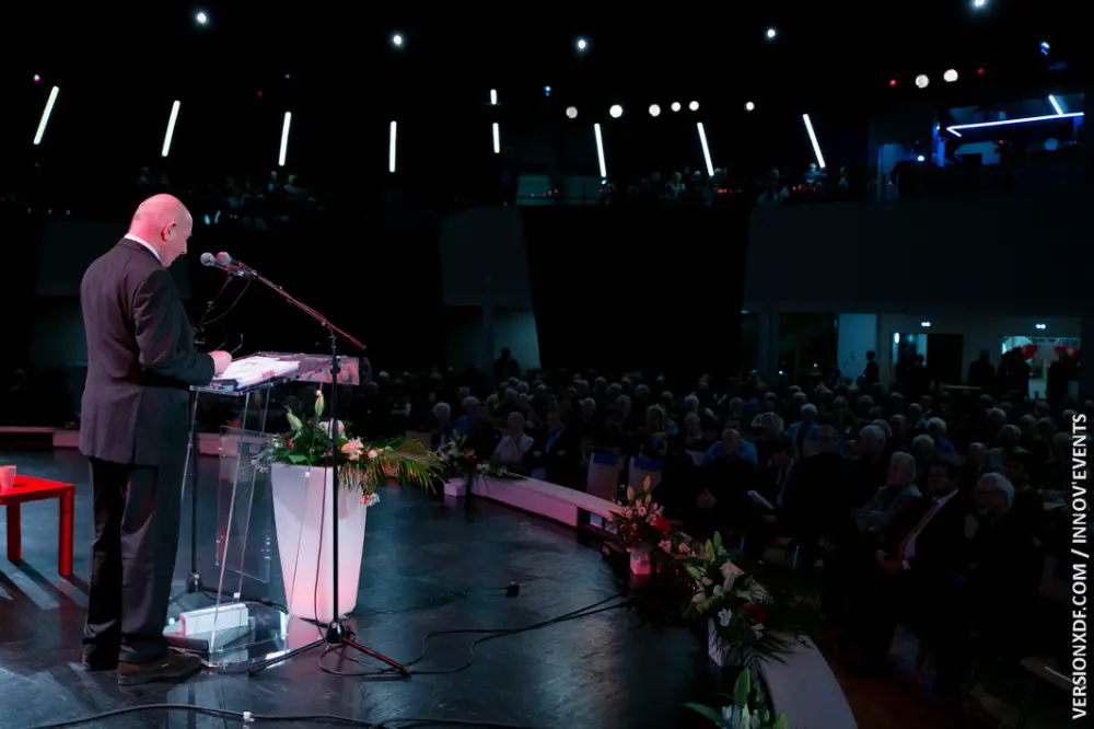 Un intervenant en costume s’exprime sur scène devant une salle comble à Toulon pendant une convention professionnelle.