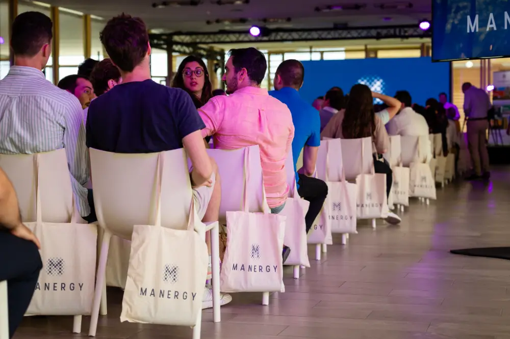 Participants assis de dos avec des sacs aux couleurs de l’événement MANERGY accrochés aux chaises