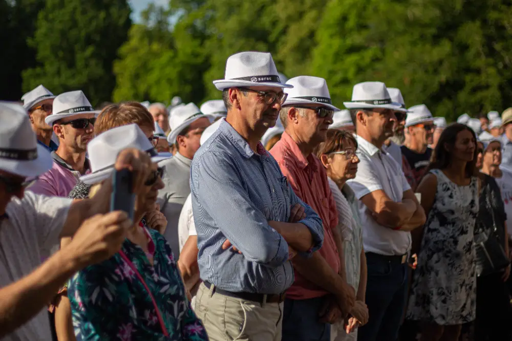 Participants portant des chapeaux blancs lors d’une convention corporate au Mans, attentifs à un discours en plein air