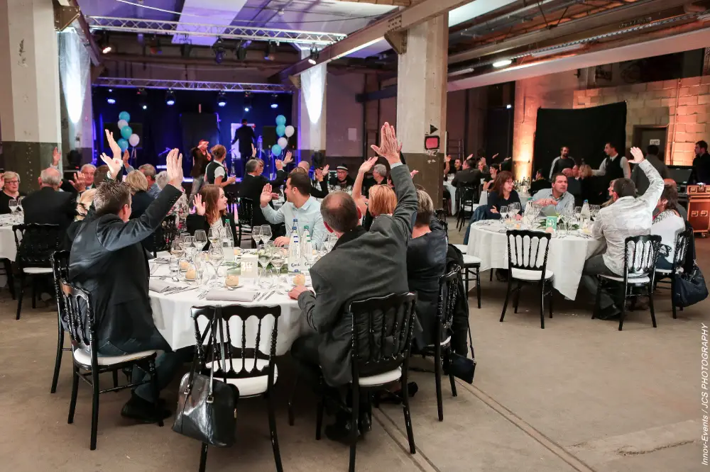 Dîner assis lors d'une convention d’entreprise à Bourg-en-Bresse, avec des participants levant la main autour de tables rondes.
