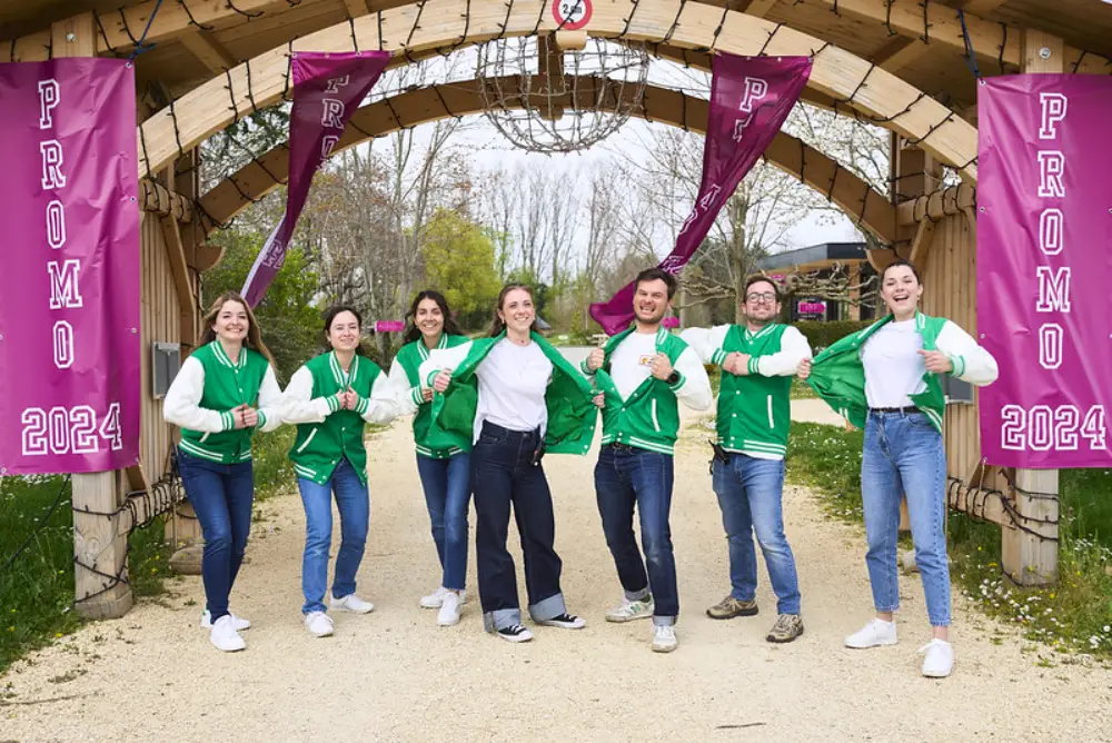 Équipe d’entreprise en vestes personnalisées posant fièrement sous une arche aux couleurs de la promotion 2024