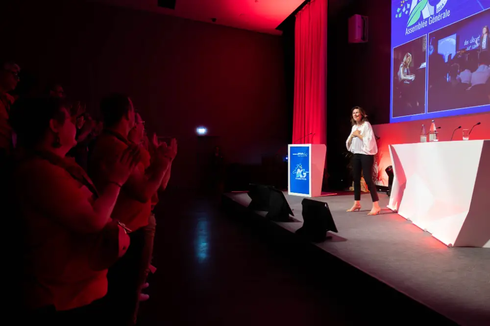 Animatrice saluée par le public sur scène lors d’un événement professionnel organisé à Genève.