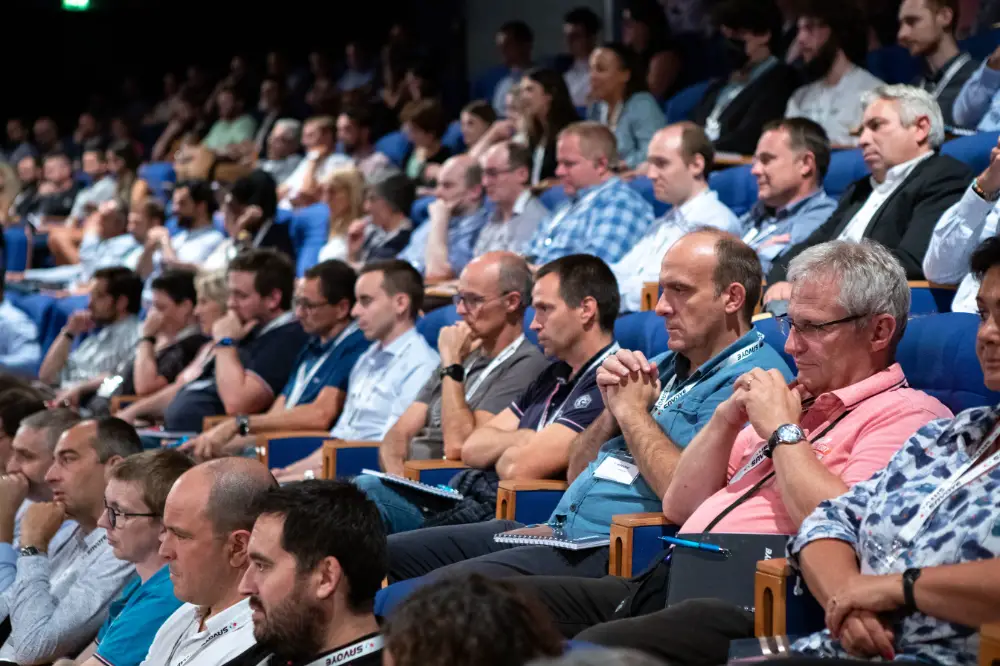 Corporate delegates focused during a conference session in a blue-seated theater